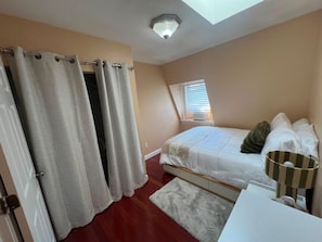 A bedroom with a bed, a window with blinds, a ceiling light, and a door with curtains. - Large 3BR/2BA - 1500sqf - Steps to Harvard (Cambridge)