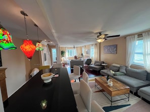 A modern living room with a dining area, a ceiling fan, and a large window with curtains. - Large 3BR/2BA - 1500sqf - Steps to Harvard (Cambridge)