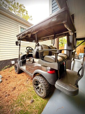 A golf cart parked in a residential driveway with a house in the background. - Ocean Lakes 3 BR. Golf Cart & Linens. Outdoor Entertainment Area. 3 Min to Beach (Myrtle Beach)