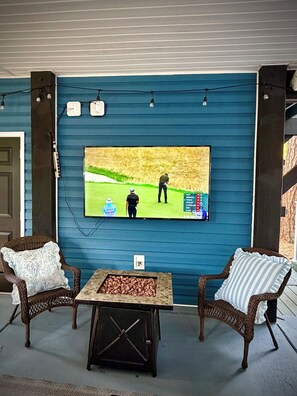 Een kamer met twee rieten stoelen, een bijzettafeltje en een flatscreen-tv aan een blauwe muur waarop een golfwedstrijd wordt getoond.