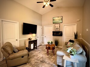 A living room with a ceiling fan, a flat-screen TV, a sofa, a chair, and a coffee table. - Ocean Lakes 3 BR. Golf Cart & Linens. Outdoor Entertainment Area. 3 Min to Beach (Myrtle Beach)