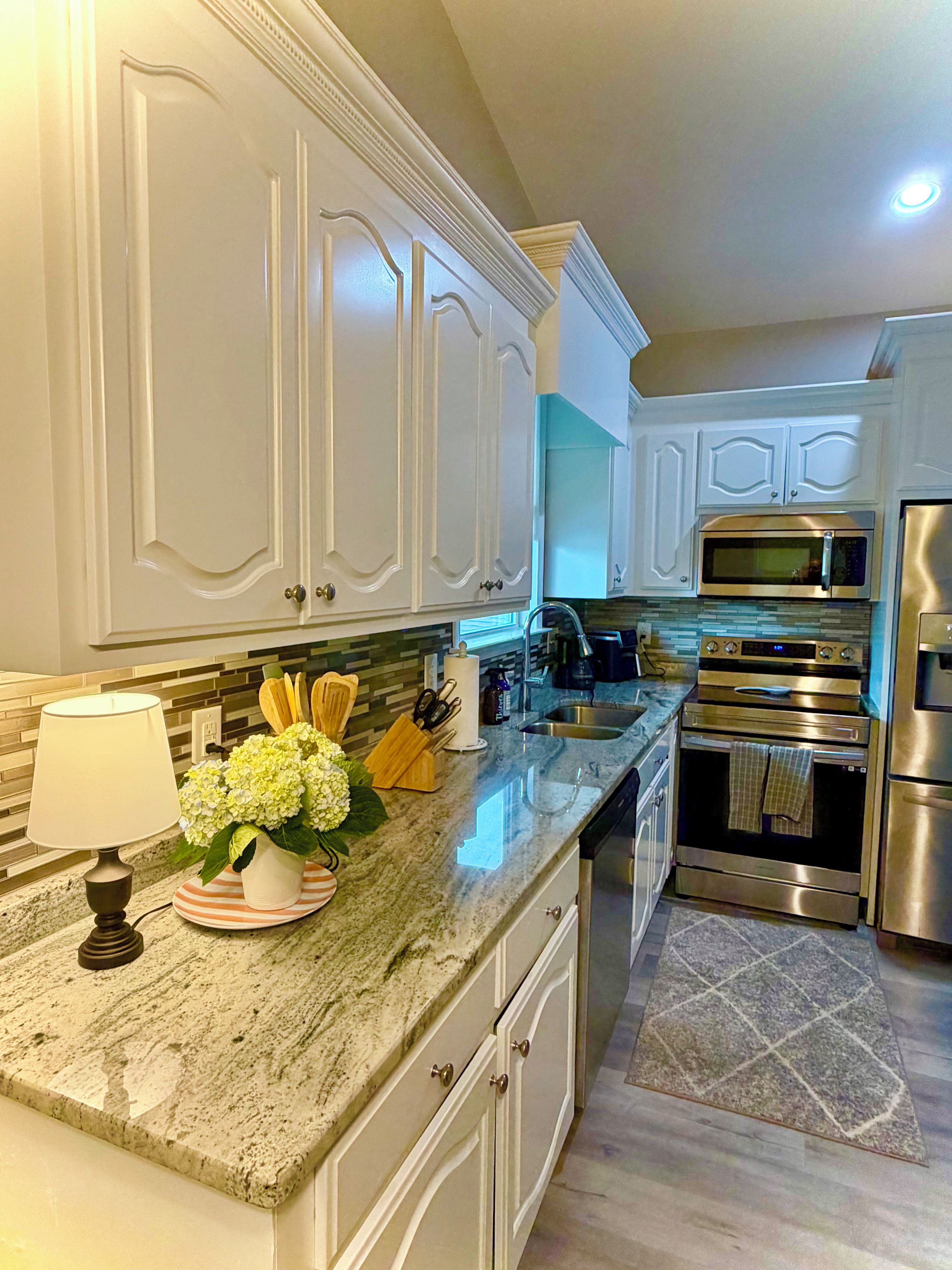 A kitchen with white cabinetry, a marble countertop, stainless steel appliances, and a decorative vase with flowers.