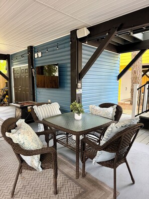 An outdoor seating area with wicker furniture and a glass table, a blue house with a wooden door, and a tree. - Ocean Lakes 3 BR. Golf Cart & Linens. Outdoor Entertainment Area. 3 Min to Beach (Myrtle Beach)