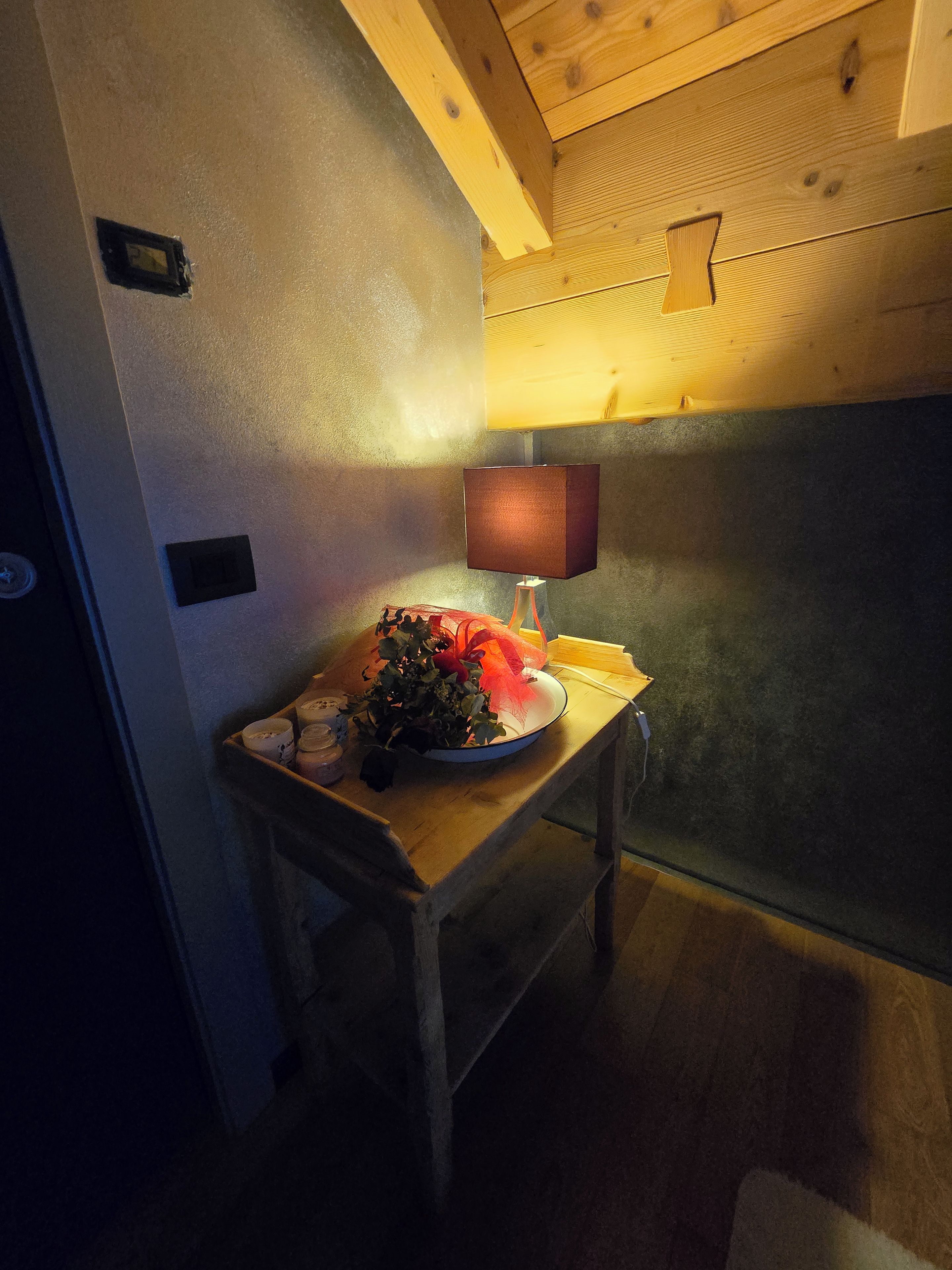 A room with a wooden table, a lamp, and a bowl of flowers.