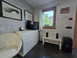 A room with a television on a dresser, a chair, a window with a view, and a speaker. - Chalet Soàndel Nature & Relax (Trentino-Alto Adige)