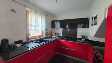 A kitchen with red cabinets, a black countertop, a window with curtains, and a stove.