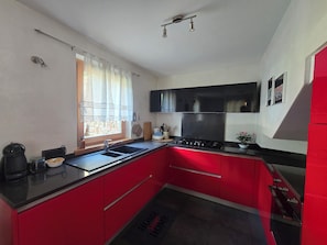 A kitchen with red cabinets, a black countertop, a window with curtains, and a stove.