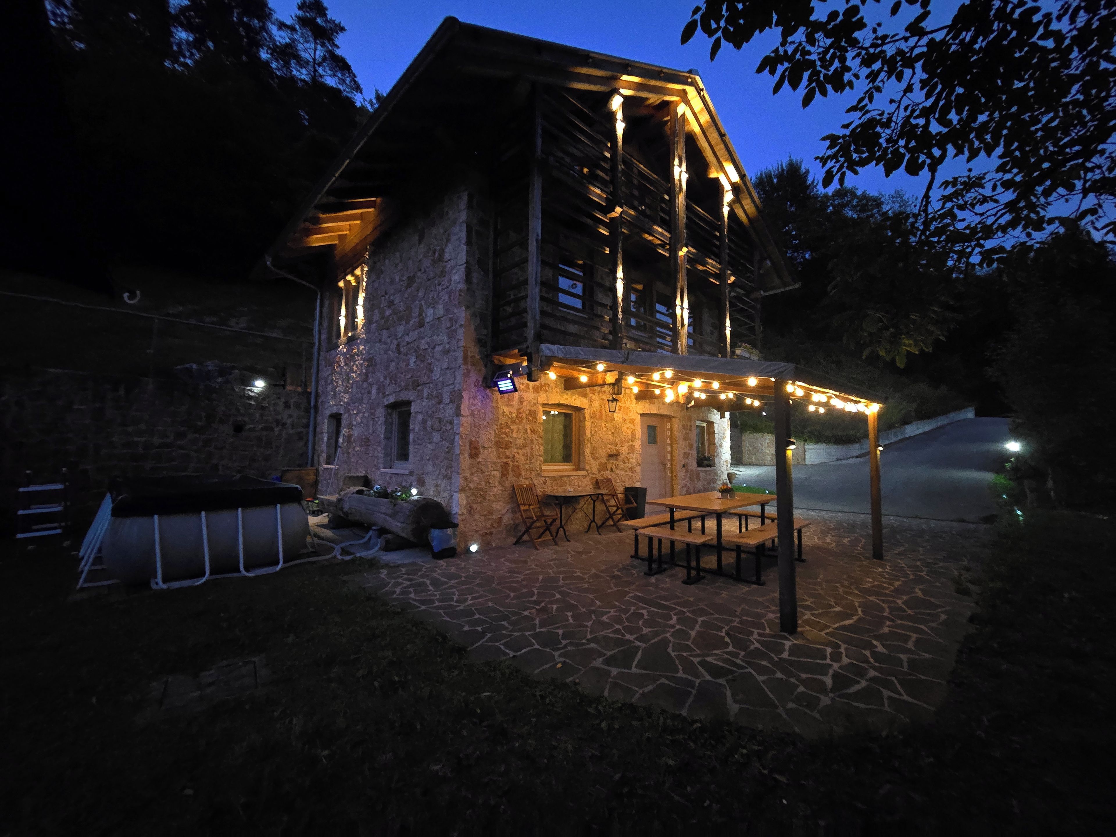 A stone building with a wooden exterior, outdoor seating, and string lights.