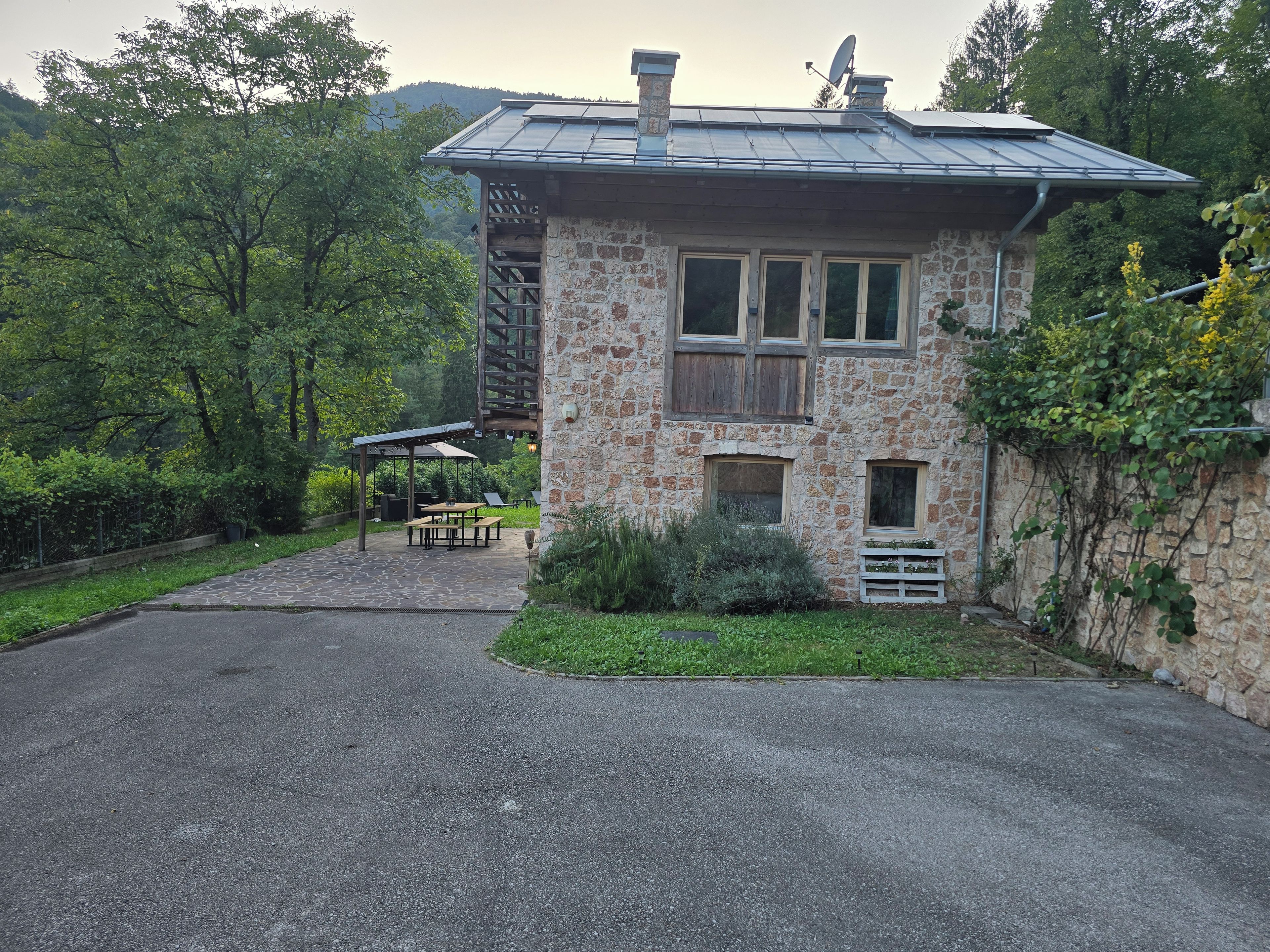 Ein Steinhaus mit Metallbedachung, einer Holzterrasse und einem gepflasterten Auffahrt.