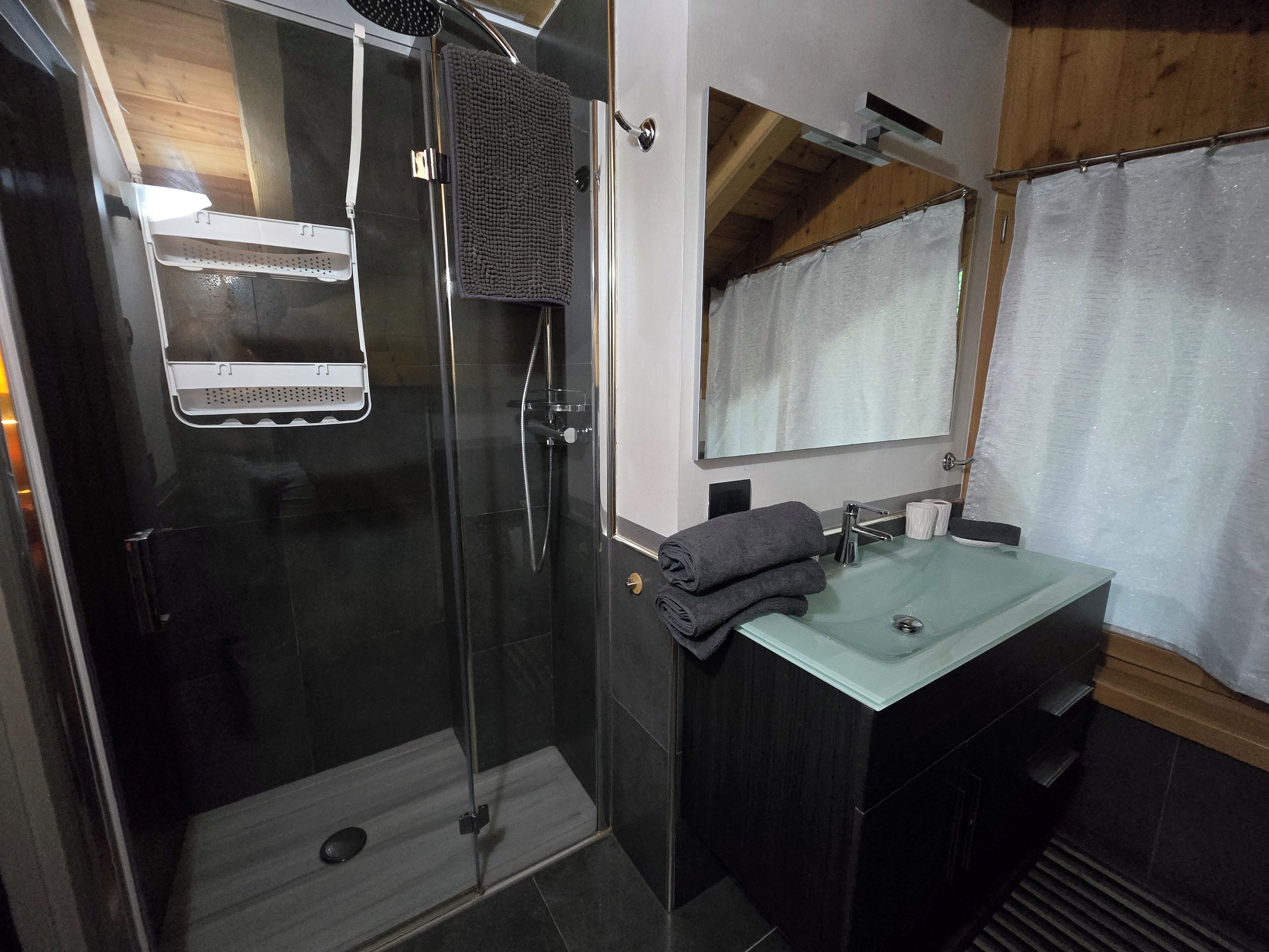 Un baño moderno con ducha envuelta en vidrio, lavamanos de cristal y espejo sobre el lavamanos.