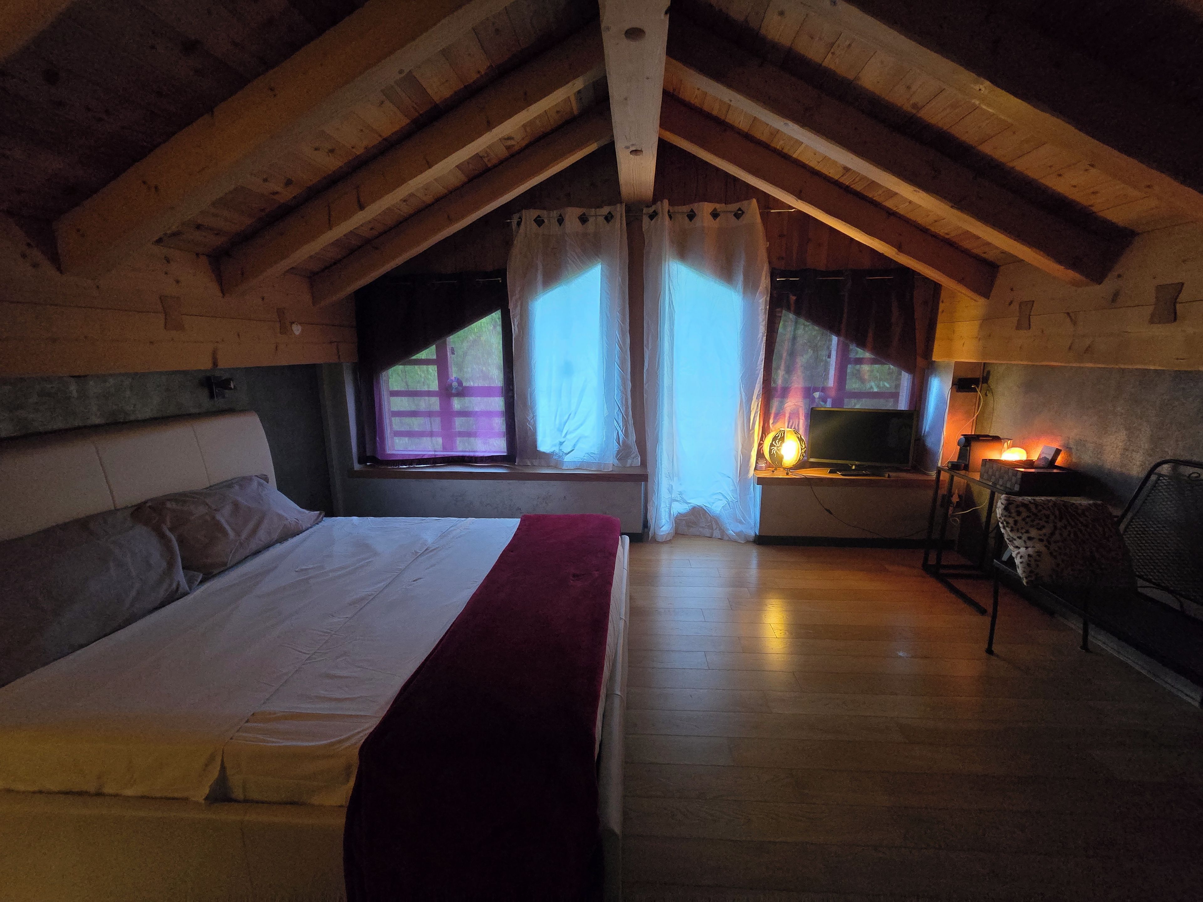 Ein Schlafzimmer mit einem Bett, einem Schreibtisch mit Lampe und einem Fenster mit Vorhängen.