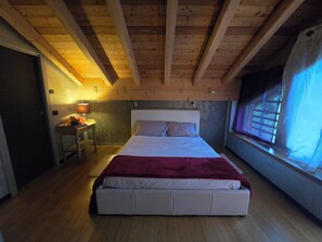 A bedroom with a wooden ceiling, a bed with white bedding and a red blanket, a bedside table with a lamp, and a window with curtains. - Chalet Soàndel Nature & Relax (Trentino-Alto Adige)