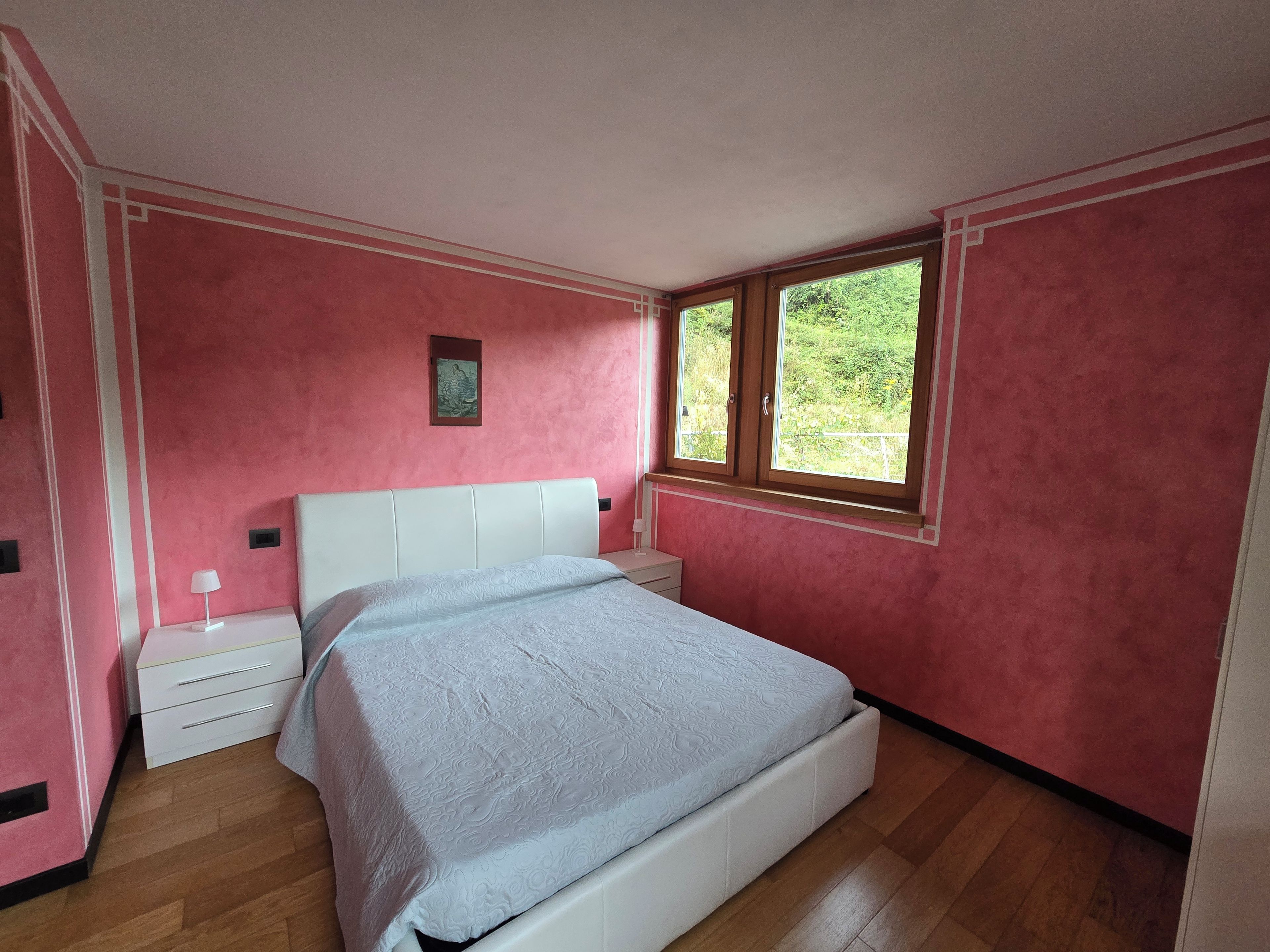 A bedroom with a bed, a nightstand, a window, and a door.