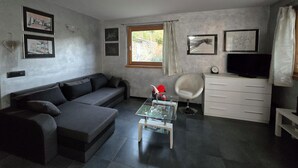 En moderne stue med en grå sofa, et glasbord, en hvid lænestol, et fjernsyn og billeder i rammer på væggen.