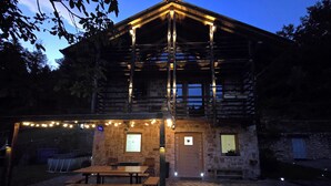 A rustic wooden building with a stone patio, outdoor seating, and string lights. - Chalet Soàndel Nature & Relax (Trentino-Alto Adige)