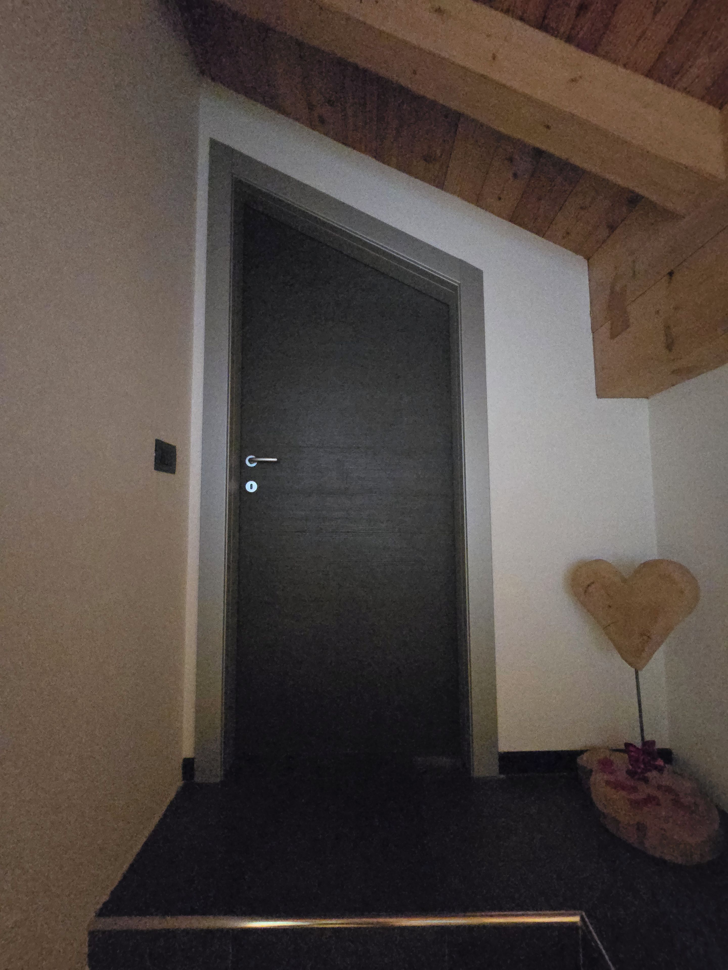 A dark wooden door with a simple handle, a heart-shaped decoration on the wall, and a small rug on the floor.