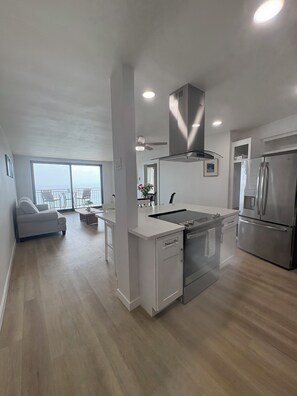 A modern kitchen with a central island, stainless steel appliances, and a view to the outside. - Luxurious Oceanfront Condo w/ Endless views and Sunsets (San Diego)