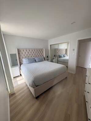 A bedroom with a large bed, a wardrobe, a mirror, and a nightstand. - Luxurious Oceanfront Condo w/ Endless views and Sunsets (San Diego)