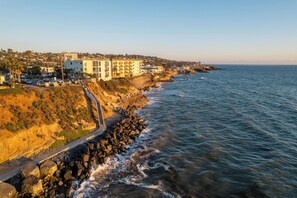 Une ville côtière, avec une route menant à un rivage rocheux, des bâtiments dotés de balcons donnant sur la mer et un ciel dégagé.