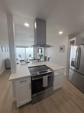 A modern kitchen with a central island, stainless steel appliances, and a view to the outside. - Luxurious Oceanfront Condo w/ Endless views and Sunsets (San Diego)