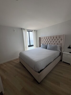 A bedroom with a large bed, a nightstand, and a window with curtains. - Luxurious Oceanfront Condo w/ Endless views and Sunsets (San Diego)