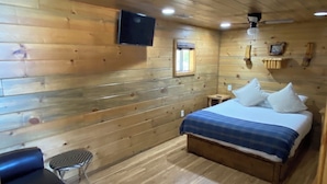 Una stanza con pannelli in legno, un letto, un tavolino, una sedia e una televisione a parete.