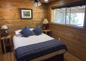 A wooden cabin bedroom with a bed, two nightstands, a lamp, and a window.