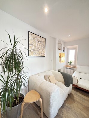 Ein modernes Wohnzimmer mit einem weißen Sofa, einer Topfpflanze und einem gerahmten abstrakten Kunstwerk.