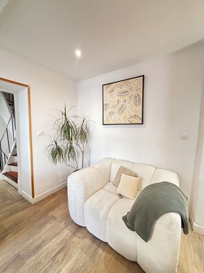 A modern living room with a white sofa, a large abstract painting, and a staircase. - Spacious, ideal 3-bedroom apartment on the harbor, right in the heart of Sanary (Sanary-sur-Mer)