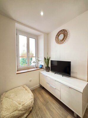 A room with a white cabinet, a flat-screen TV, a window with a view, a round mirror, and a fluffy ottoman. - Spacious, ideal 3-bedroom apartment on the harbor, right in the heart of Sanary (Sanary-sur-Mer)