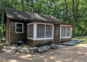 A wooden cabin with a porch, a grill, and a window labeled 'CEDARWOOD.'