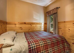 A wooden-paneled room with a bed, a window with curtains, and a view of greenery outside.