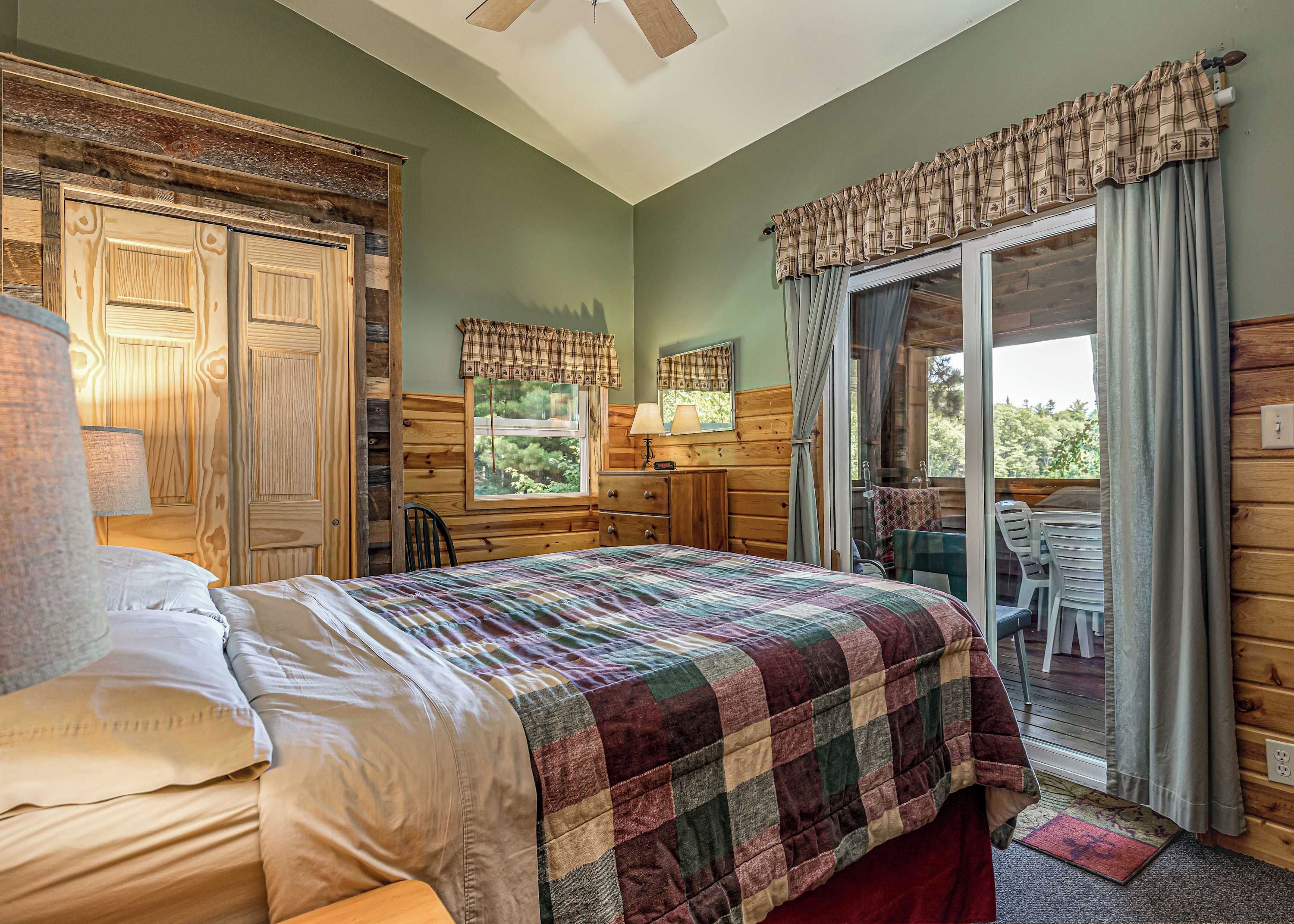 Quarto com cama, cômoda, janela com cortinas, cadeira e vista para o exterior.