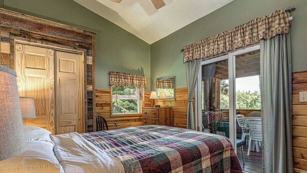 Un dormitorio con cama, cómoda, ventana con cortinas, una silla y vista al exterior.