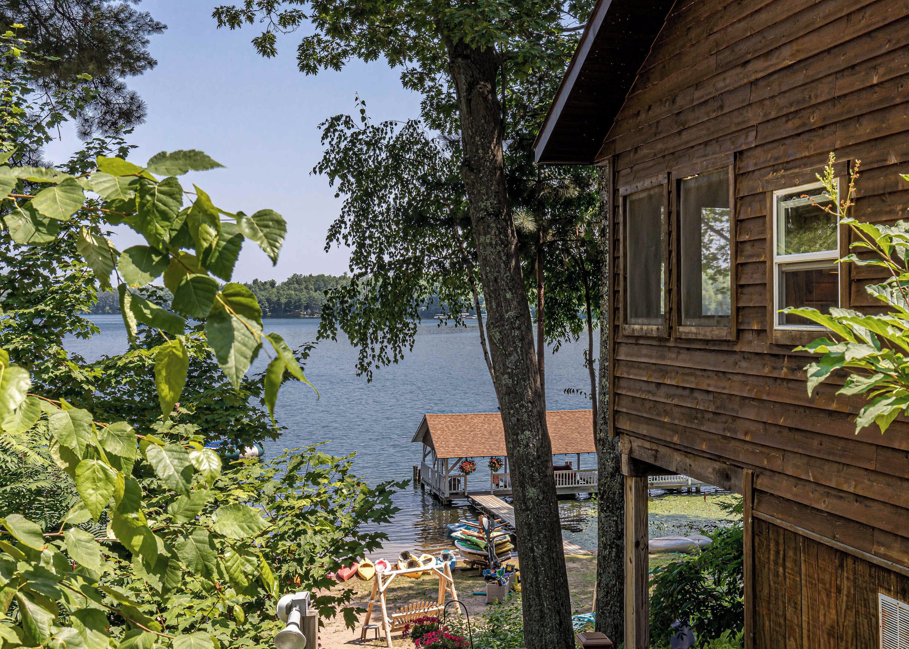 A wooden cabin with a dock extending into a lake, surrounded by trees and greenery.
