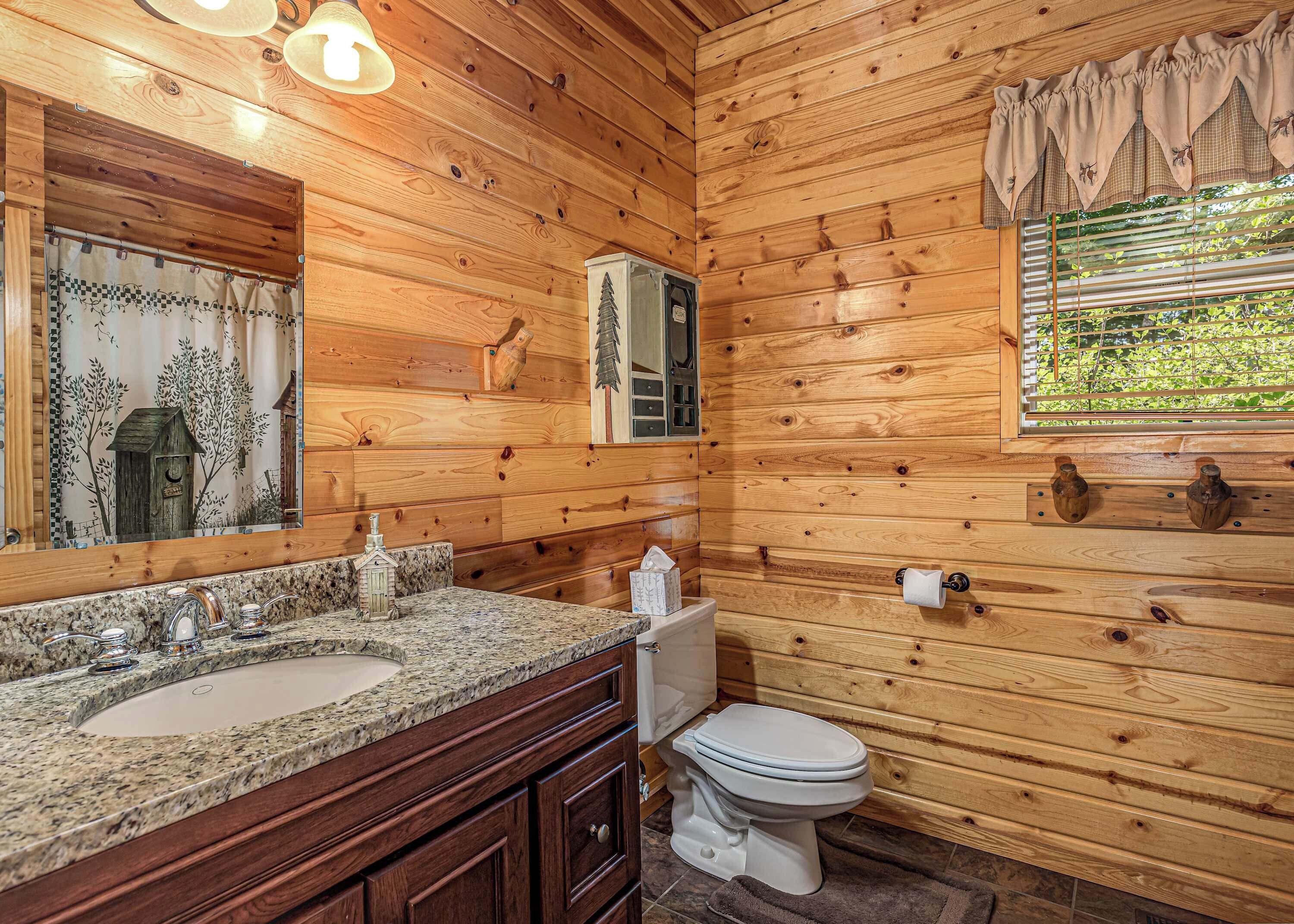 A wooden cabin bathroom with a granite countertop sink, a toilet, and a window with a view of greenery.