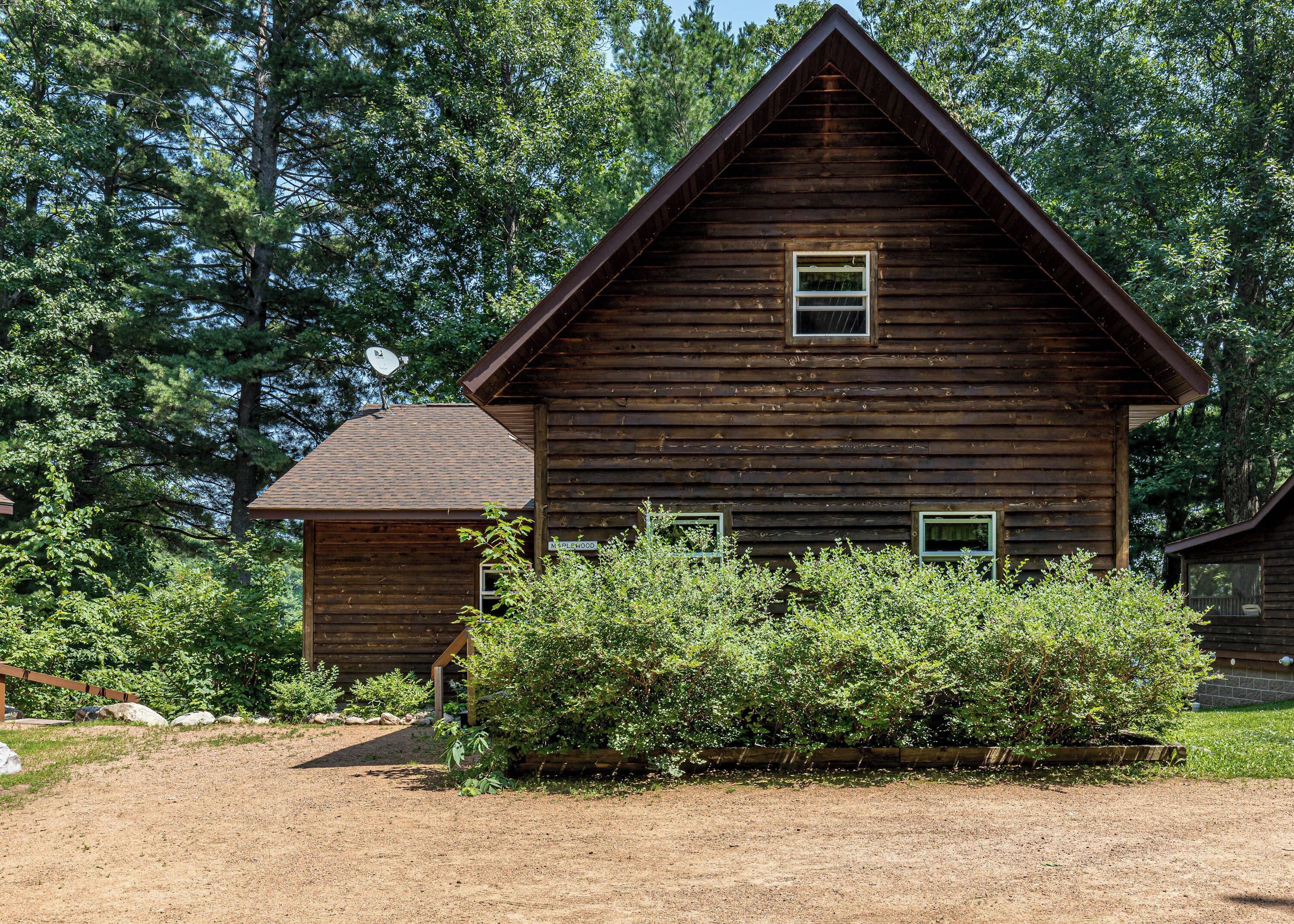 A wooden cabin with a gabled roof, surrounded by dense greenery and trees.