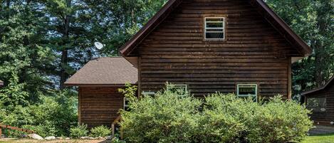 A wooden cabin with a gabled roof, surrounded by dense greenery and trees.