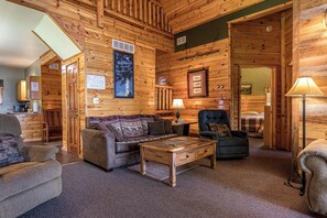Interior de uma cabana de toras com sala de estar, área de refeições e quarto.