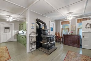 Une cuisine avec un four ancien, des armoires vertes et un coin repas comprenant une table et des chaises en bois.