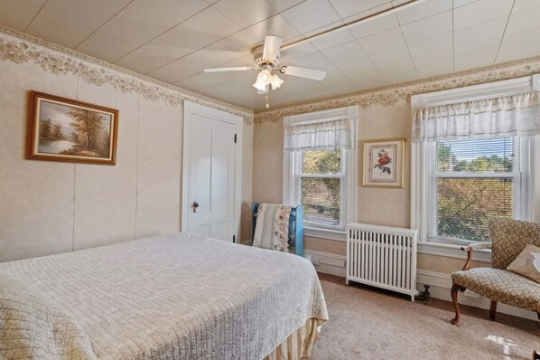 Une chambre à coucher avec un lit, une chaise, un radiateur et un ventilateur de plafond.