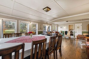 Un vaste espace dédié à la salle à manger, avec une longue table, de nombreuses chaises et une vue sur l’extérieur grâce à de grandes fenêtres.