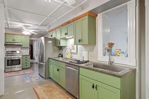 Une cuisine avec des meubles de couleur verte, des appareils en acier inoxydable, une fenêtre offrant une belle vue et un tapis à motifs.