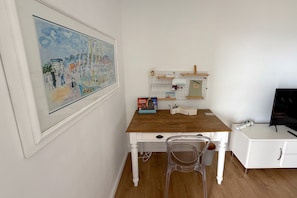 Una habitación con un escritorio de madera, una silla, un panel de corcho con objetos y un cuadro en la pared.