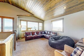 A cozy living room with a wooden ceiling, a leather sectional sofa, a bean bag, and large windows offering a view. - The Pirate Ship Chalet (Fish Haven)