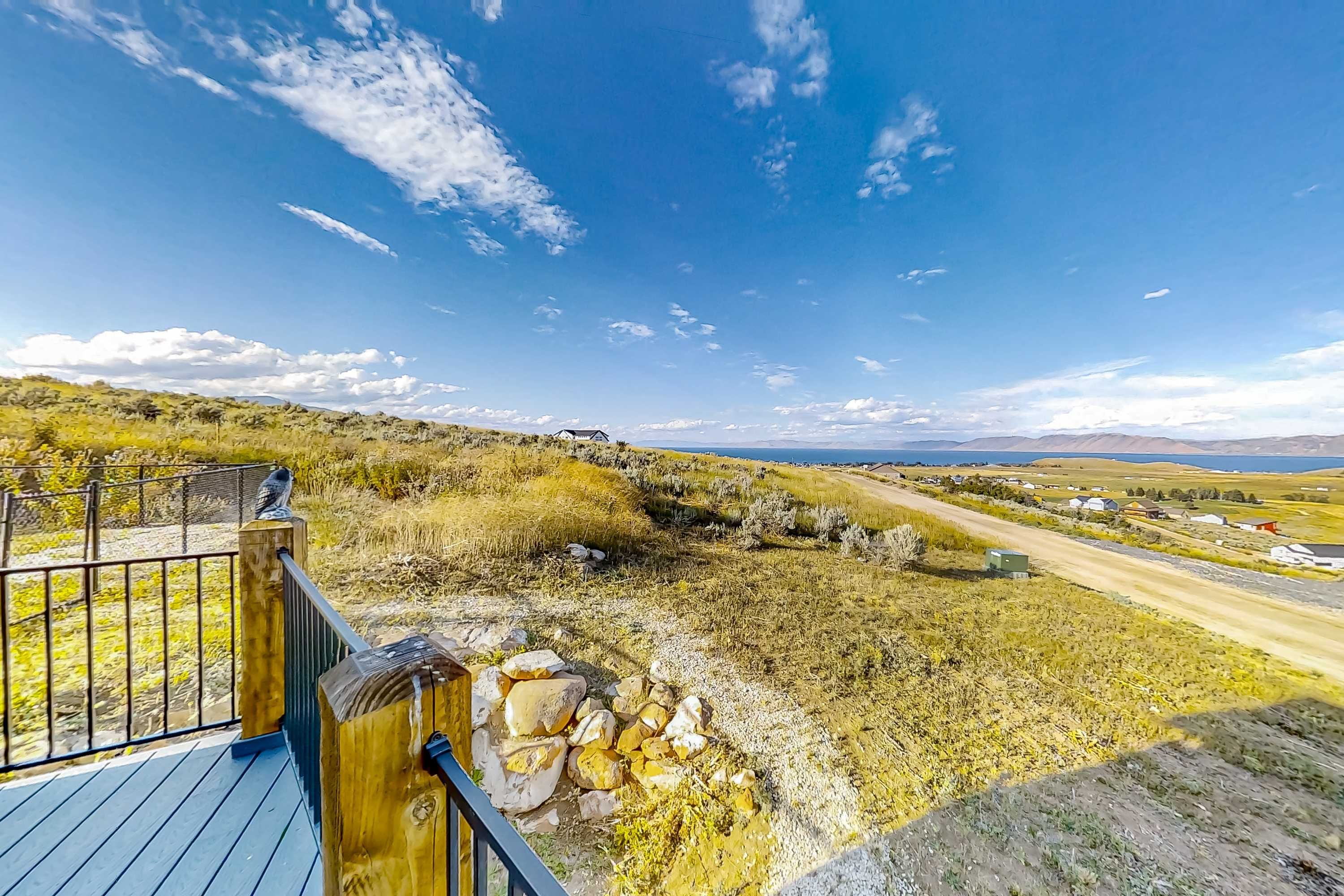 A scenic overlook with a wooden deck, a stone wall, and a view of a rural landscape with a road and distant hills.