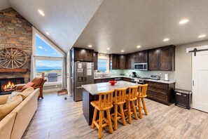 A modern kitchen with dark wood cabinets, a central island with bar stools, a built-in microwave, and a refrigerator. - Serenity w/ Ideal Beach Access! (Garden City)