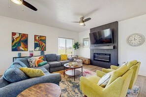 Ein modernes Wohnzimmer mit einer Couch, Sesseln, einem Couchtisch, einem Kamin, einem Fernseher und abstrakter Wandkunst.