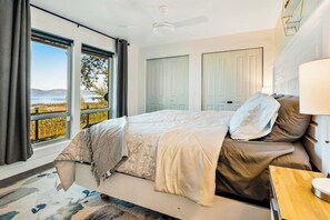 A bedroom with a bed, a nightstand, a lamp, and a view of the outdoors. - On the Waterfront - Lakefront with Mountain Views (Fish Haven)