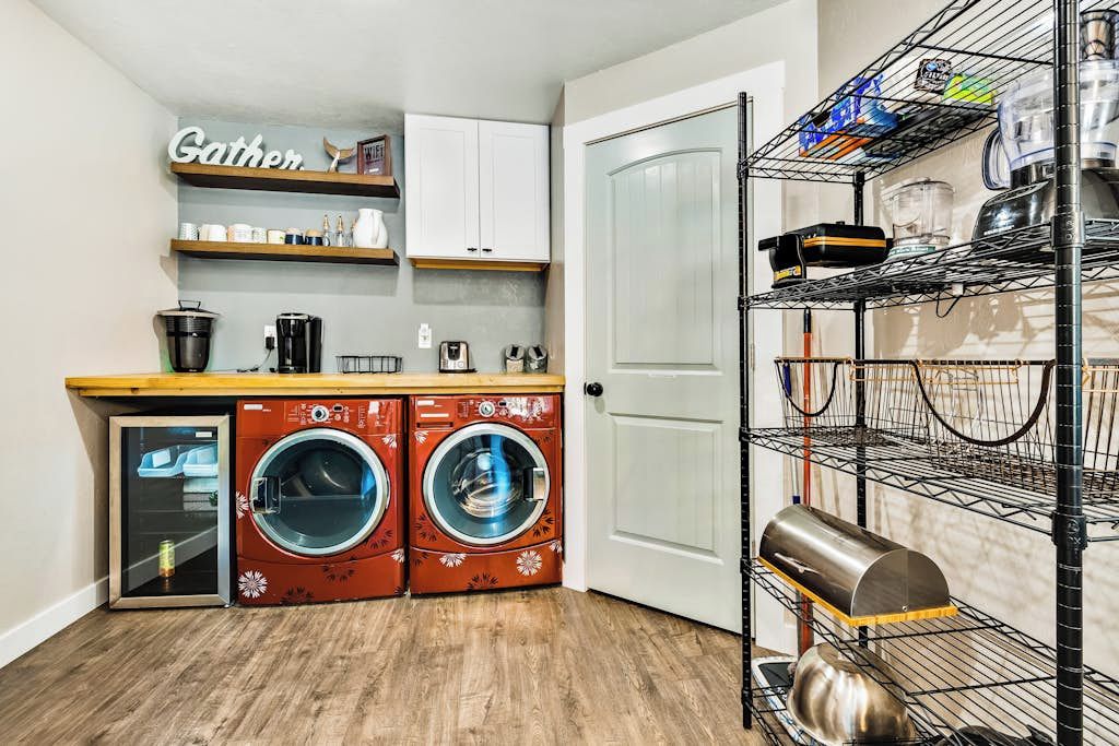 A compact kitchen with a washing machine, a coffee maker, and a shelf with kitchenware.